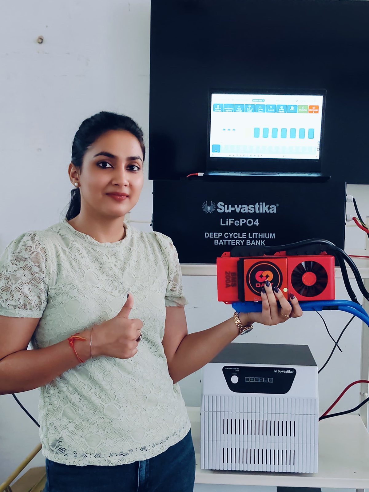 Su-vastika engineer holding a 200A BMS module in front of a LiFePO4 deep-cycle lithium battery bank with its live monitoring dashboard